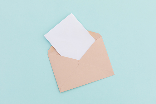 Opened brown envelope with white letter lying over pale blue background. greetings message copy space.