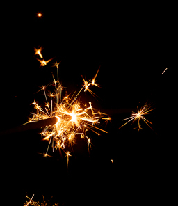 Sparkler with multiple glowing gold yellow and orange sparks on black background. Colour New Years Eve party and celebration concept.
