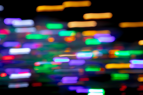 Multiple multi coloured green, orange, purple out of focus spots of light fairy lights in motion blur on black background. Colour, Christmas and celebration concept.
