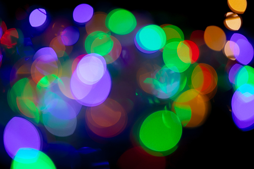 Multiple multi coloured green, orange, purple out of focus spots of light fairy lights on black background. Colour, Christmas and celebration concept.