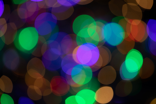 Multiple multi coloured green, orange, purple out of focus spots of light fairy lights on black background. Colour, Christmas and celebration concept.
