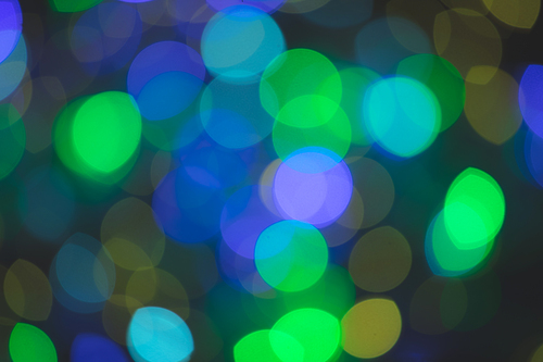 Multiple multi coloured green, blue, purple out of focus spots of light fairy lights on black background. Colour, Christmas and celebration concept.