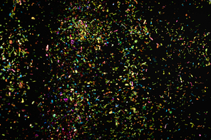 Multiple multi coloured pink yellow blue and green confetti flying and floating on black background. Colour New Years Eve party and celebration concept.
