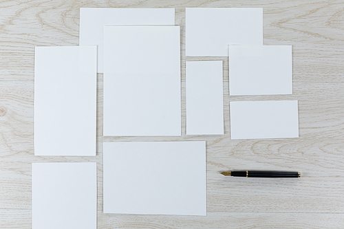 Top view of a variety of stationery pieces of white paper in various sizes, arranged on a textured wooden surface.