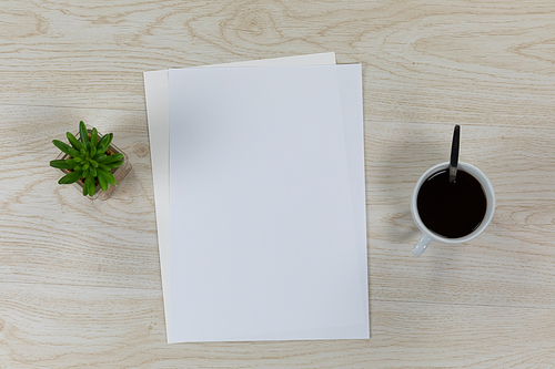 Top view of a variety of stationery pieces of white paper in various sizes, arranged on a textured wooden surface with a cup of black coffee and a plant.