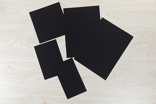Top view of a variety of sheets of black paper in various sizes, arranged on a textured white wooden surface.