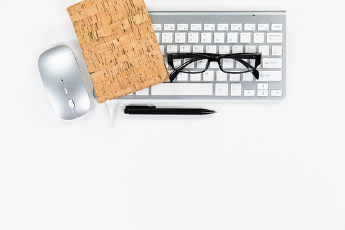 Close up top view of a computer mouse, a pen, a keyboard and glasses arranged on a plain white background