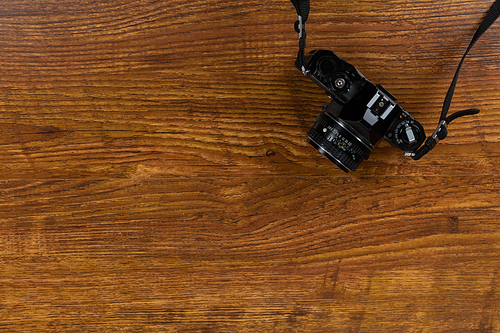Close up top view of a black digital SLR camera arranged on a textured wooden surface