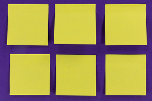 Close up top view of six yellow paper sticky memo notes in one size, arranged on a plain purple background