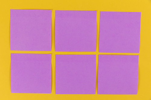 Close up top view of six purple sheets of paper sticky memo notes in one size, arranged on a plain yellow background