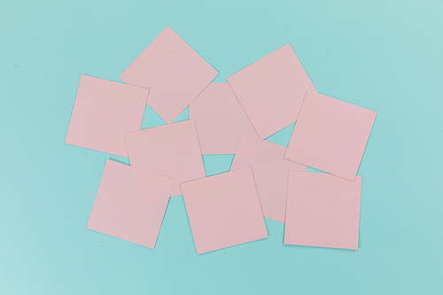 Close up top view of ten pink sheets of paper sticky memo notes in one size, arranged on a plain blue background