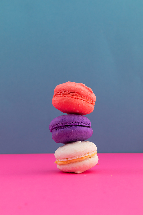 Close up of white, purple and pink macarons stacked on pink and blue background. fresh dessert fun food copy space concept.