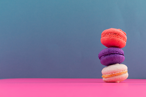 Close up of white, purple and pink macarons stacked on pink and blue background. fresh dessert fun food copy space concept.