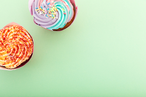 High angle view of two colourful cupcakes with sprinkles on green background. food dessert fun copy space concept.