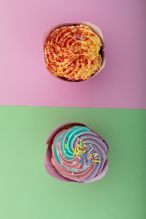 High angle view of two colourful cupcakes with sprinkles on purple and green background. food dessert fun copy space concept.