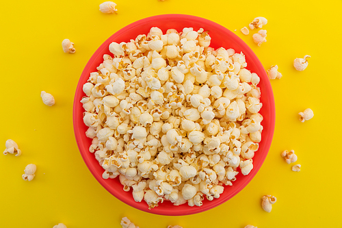 High angle view of popcorn in red bowl on yellow background. fun party food sweet treat snack concept.