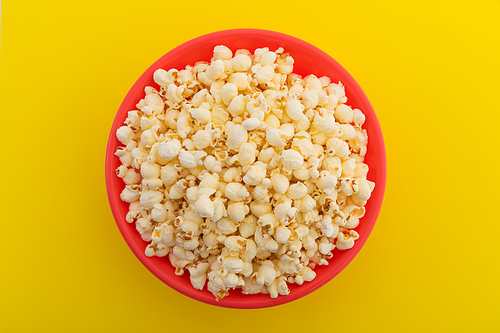 High angle view of popcorn in red bowl on yellow background. fun party food sweet treat snack concept.