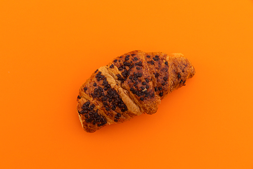 High angle view of chocolate croissant on orange background. fresh bakery breakfast food copy space concept.