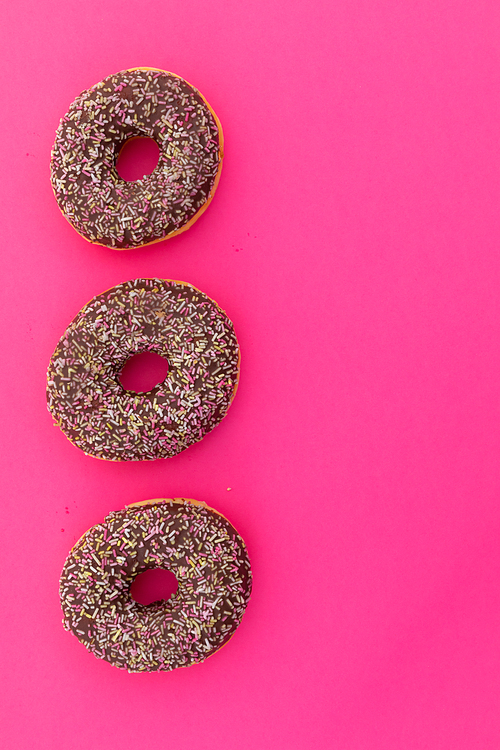 High angle view of three chocolate donuts with sprinkles on pink background. fresh bakery desert sweet food copy space concept.