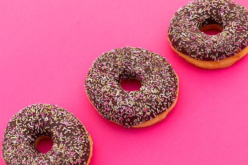 High angle view of three chocolate donuts with sprinkles on pink background. fresh bakery desert sweet food copy space concept.
