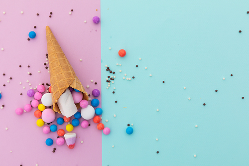 Ice cream cone and scattered colourful sprinkle on pink and blue background. fresh dessert fun food copy space concept.