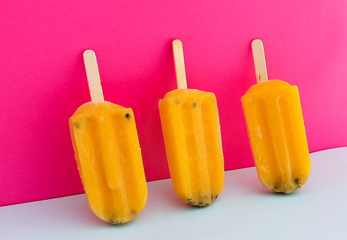 Close up of three yellow ice lollipops upside down on pink background. food dessert summer fun concept.