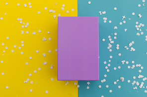 Purple gift box and white confetti on yellow and blue background. happy birthday party celebration giving receiving concept.