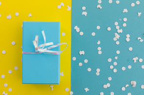 Blue gift box with ribbon and white confetti on yellow and blue background. happy birthday party celebration giving receiving concept.