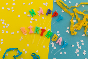 Happy birthday candles with confetti and party streamers on blue and yellow. happy birthday party fun concept.