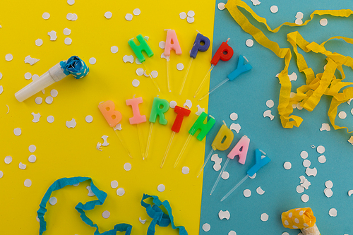 Happy birthday candles with confetti and party streamers on blue and yellow. happy birthday party fun concept.