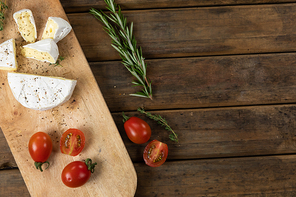 Top view of a wooden cutting board with cherry tomatoes and cheese arranged on a on a textured wooden surface with a spring of thyme.