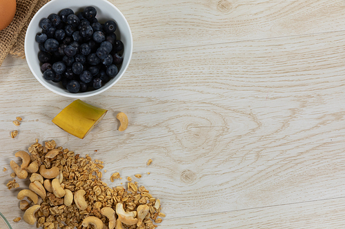 Top view of a variety of nuts and muesli and a bowl of fresh berries, arranged on a textured wooden surface.