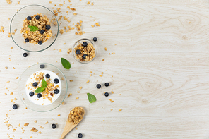Top view of three bowls with muesli, nuts, blueberries and yoghurt, arranged on a textured white wooden surface.
