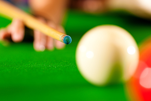 Somebody in a billiard hall playing Billiard|just hands to be seen|focus is on tip of cue