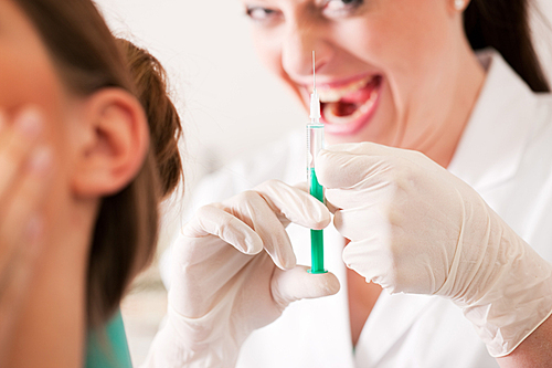 At the dentist - a female patient is getting ready to receive a anesthetization syringe|the nurse has a very disturbing diabolic smile (focus on hand of nurse)