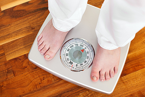 Woman (only feet to be seen) standing on bathroom scale measuring her weight controlling her dieting results