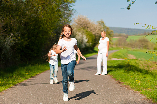kids running down a path in spring|their pregnant mother standing in the background