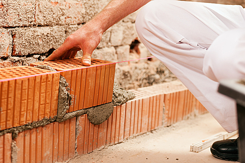 bricklayer laying|well|bricks to make a wall|he is pulling grout out of a joint with his trowel. This man is really working hard.