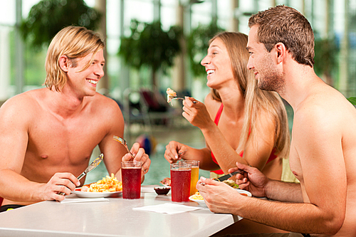 Three young people - woman and two men - eating and drinking in a restaurant at a public swimming pool
