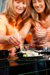 Mother and adult daughter eating sushi at home - FOCUS is on the hands