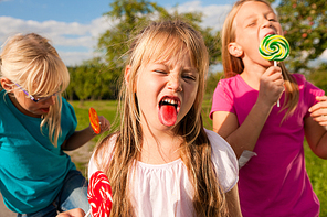 Three girls eating lollipops|the girl in front sticking her tongue out