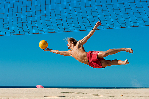 Man playing beach volleyball diving after the ball under a clear blue sky