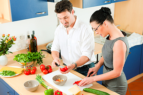 Young couple - man and woman - cooking in their kitchen at home preparing vegetables for salad and pasta sauce