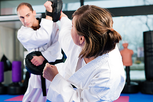 People in a gym in martial arts training exercising Taekwondo|both have a black belt