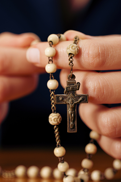Woman (only closeup of hands to be seen) with rosary sending a prayer to God|the dark setting suggests she is sad or lonely