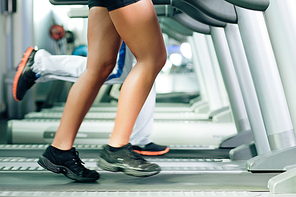 Woman and man in gym - only legs to be seen - exercising running on the treadmill to gain more fitness; motion blur in limbs for dynamic