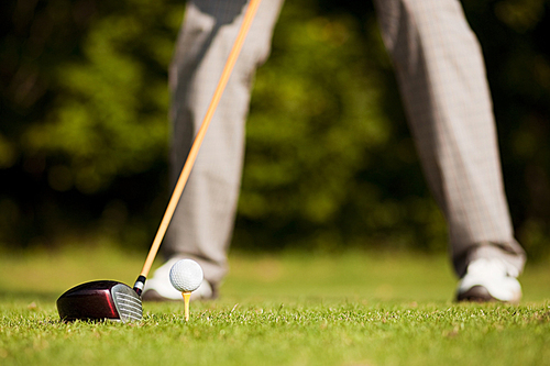 Golf player attempting the tee stroke in the teeing area (only legs of player to be seen|focus on ball)