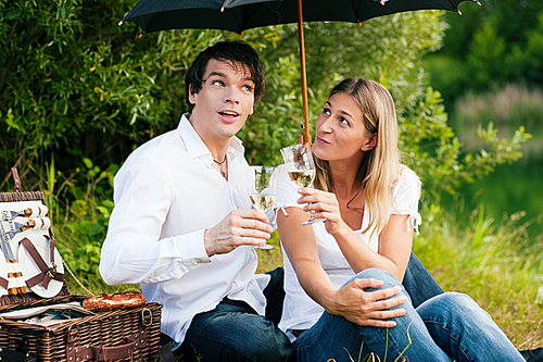 Couple in love sitting on a lake having a picnic with wine - it is starting to rain but they do not care much