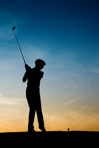 Senior woman playing golf - pictured as a silhouette against an evening sky