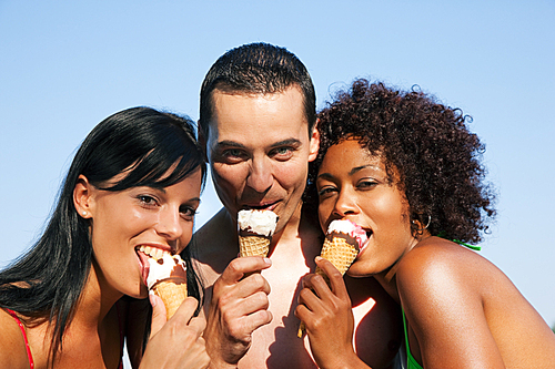 Group of friends - one man and two women eating ice cream in swimwear and bikini|it seems to be a hot summer day